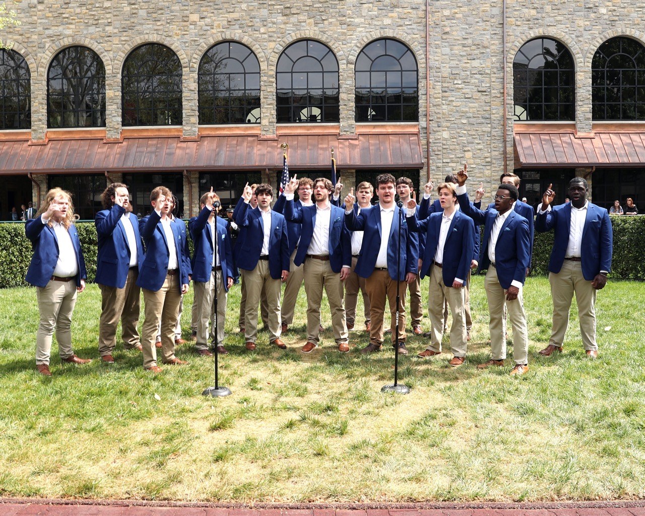The acoUstiKats performing outdoors in blue blazers in front of a stone building.
